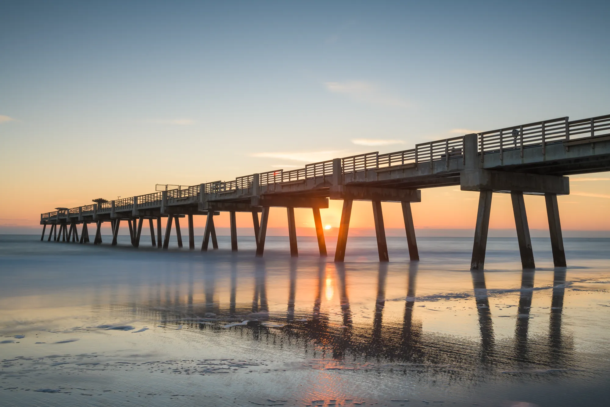The Jacksonville Beach pier at sunset, the sun setting through the pilings