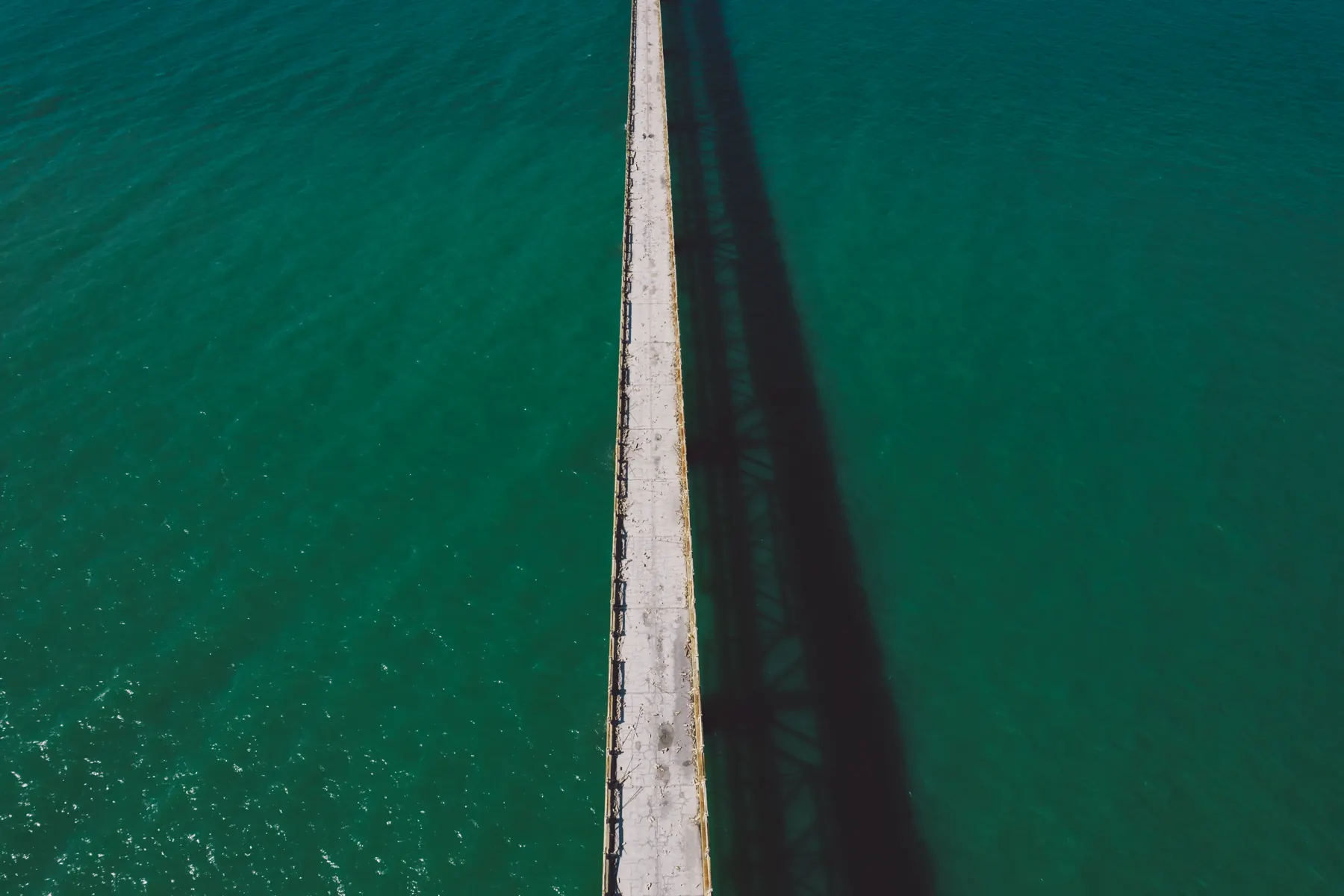 A pier reaching out over clear green water, seen from directly above