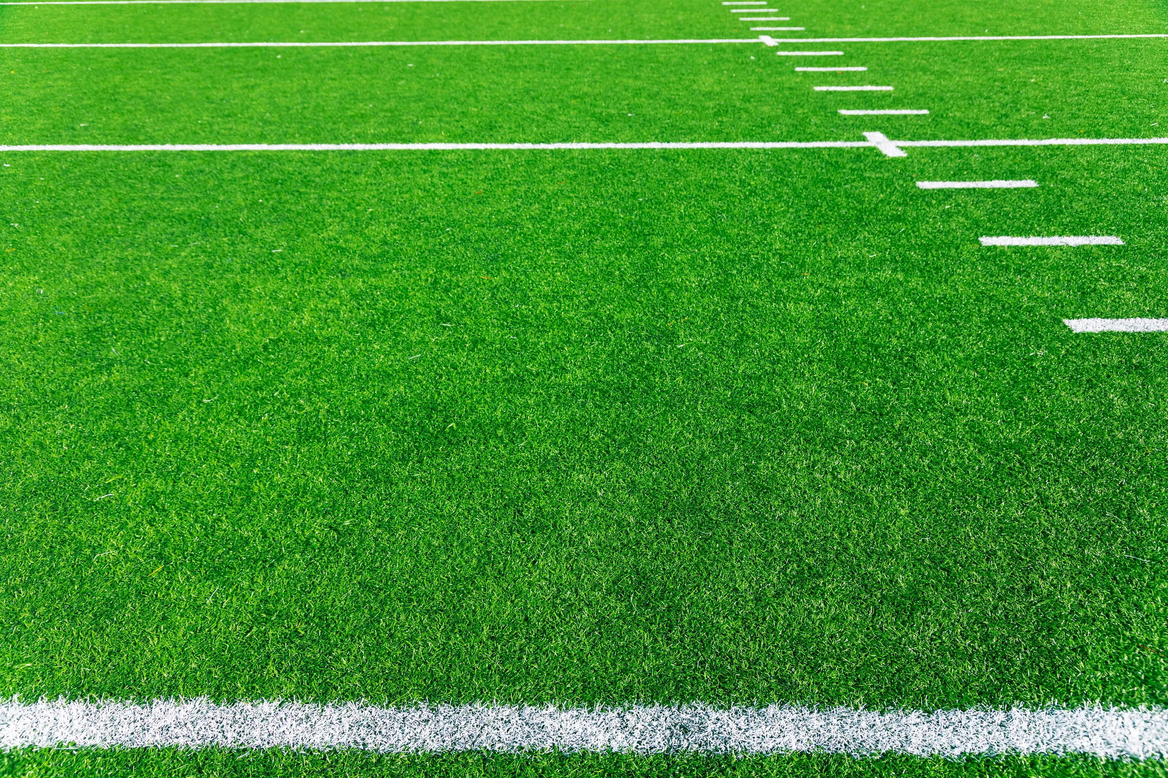 Bright green football turf with yard markers and the white sideline
